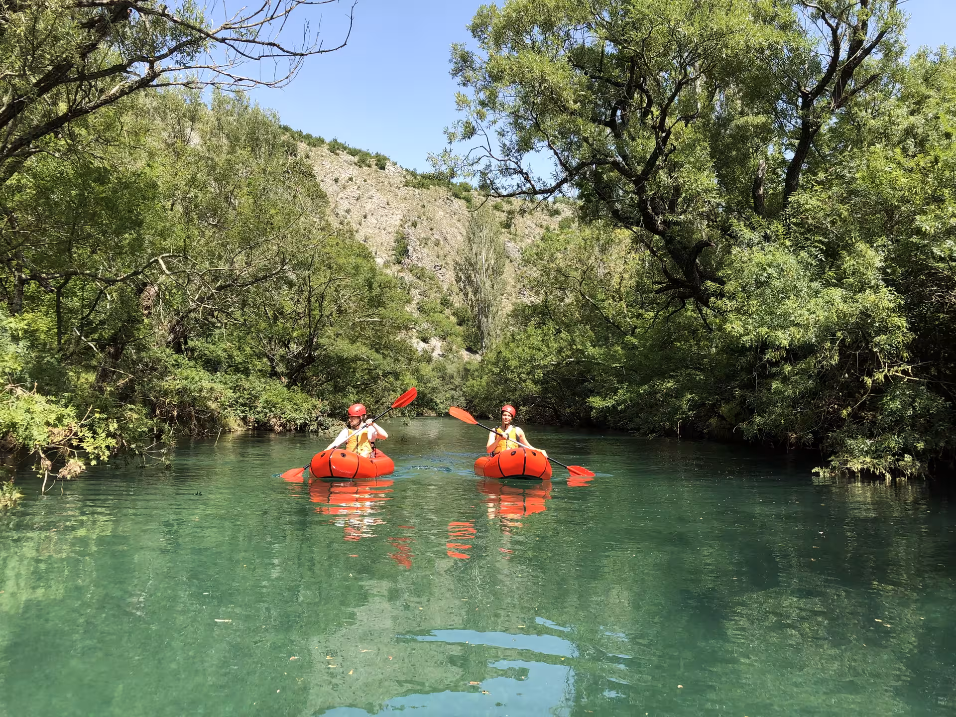Adventurers packrafting on the serene Zrmanja River surrounded by lush green landscapes and clear waters.