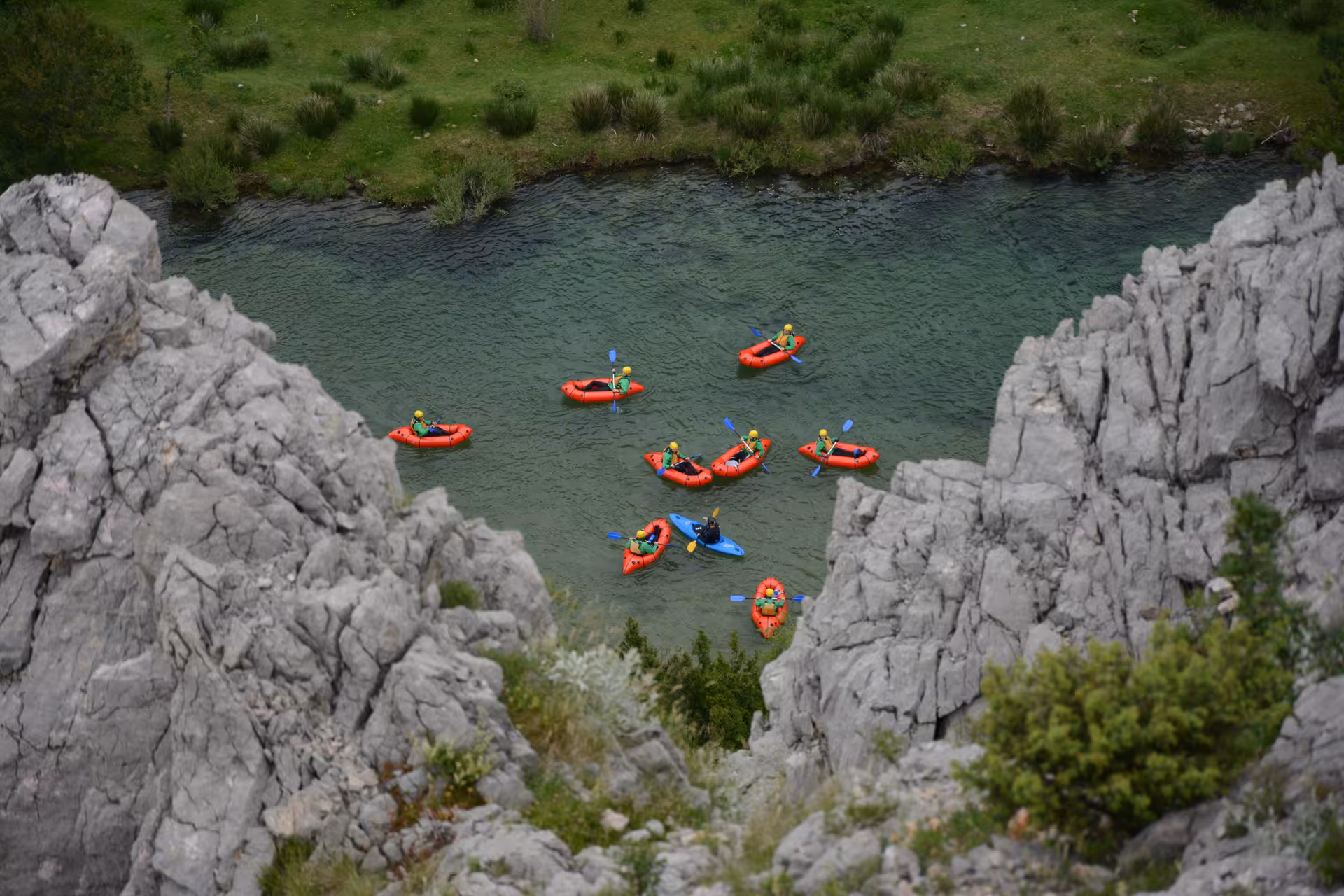 Bird's-eye view of a group packrafting adventure on the Zrmanja River amidst rocky cliffs and lush greenery.