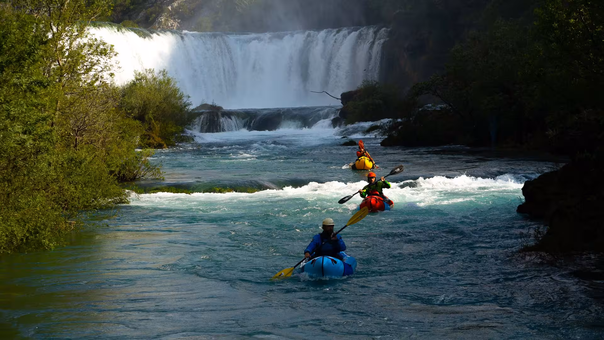 Group of packrafters navigating rapids near a stunning waterfall on the Zrmanja River, ideal for adventure seekers.