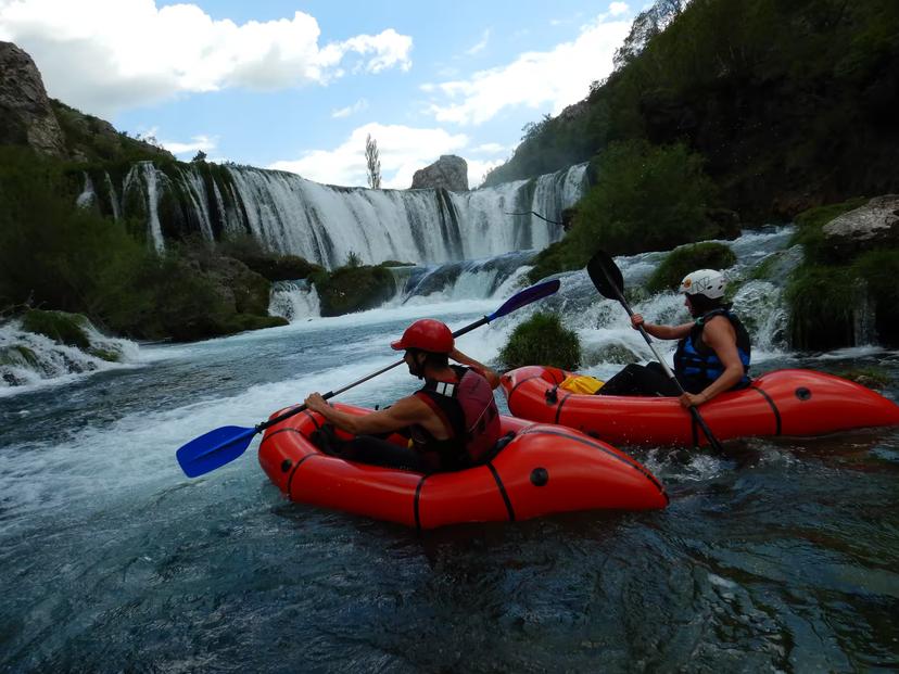 Two adventurers packrafting on the scenic Zrmanja River near cascading waterfalls, perfect for outdoor enthusiasts.