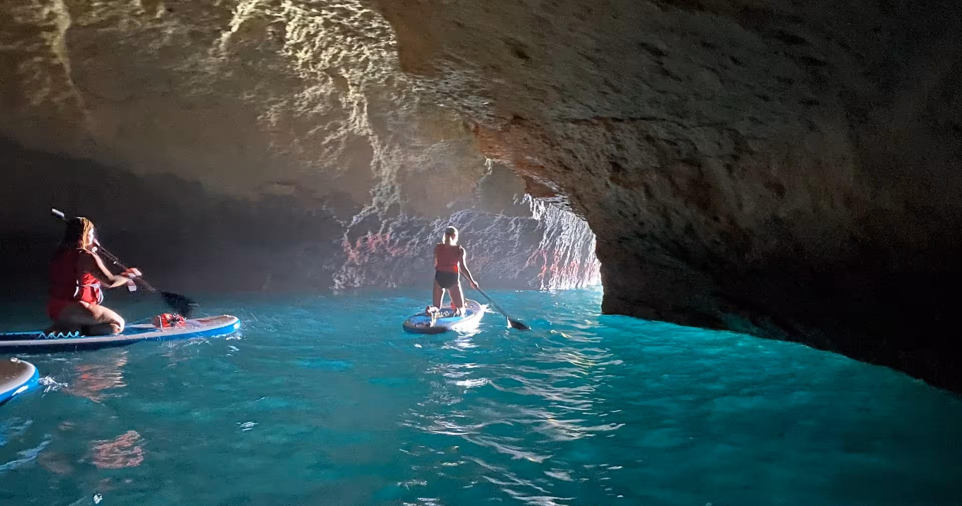 Paddleboarders explore glowing turquoise water inside Benagil sea cave at sunrise on a guided Algarve SUP tour