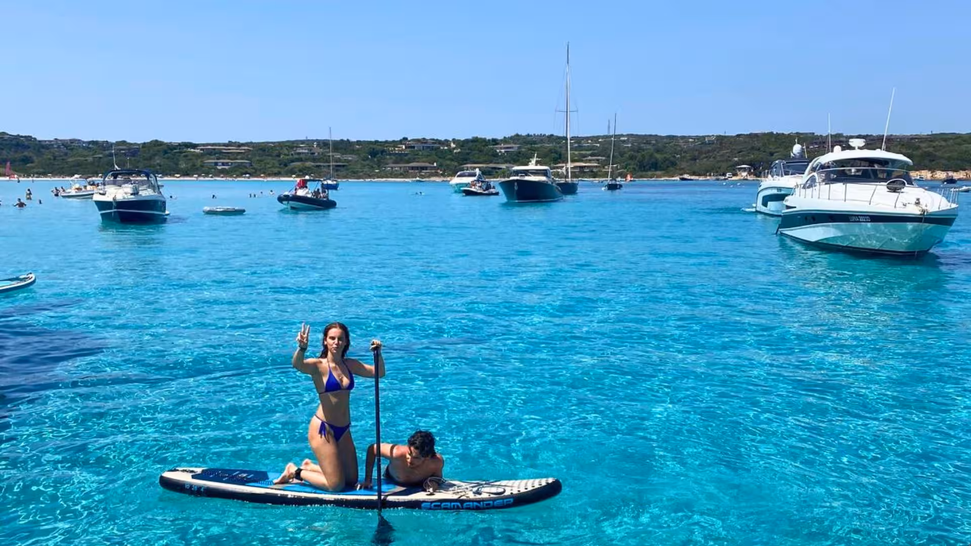 Tourists enjoying paddleboarding amidst boats on the clear turquoise sea in southern Corsica.