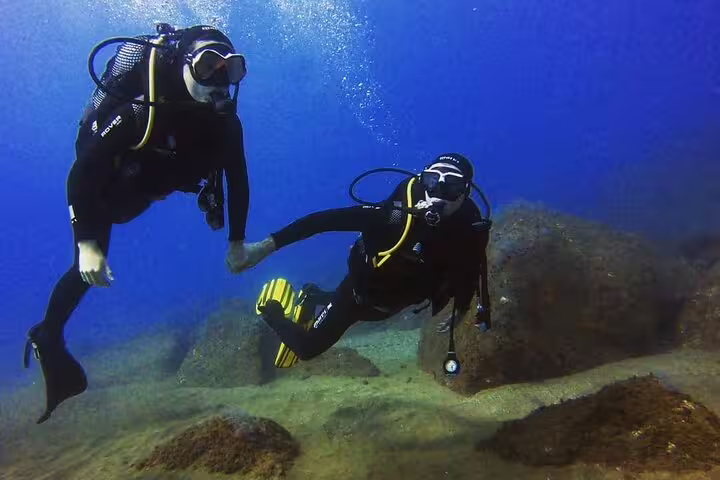 Two scuba divers explore vibrant underwater scenery holding hands during an Open Water Course, showcasing marine adventure.
