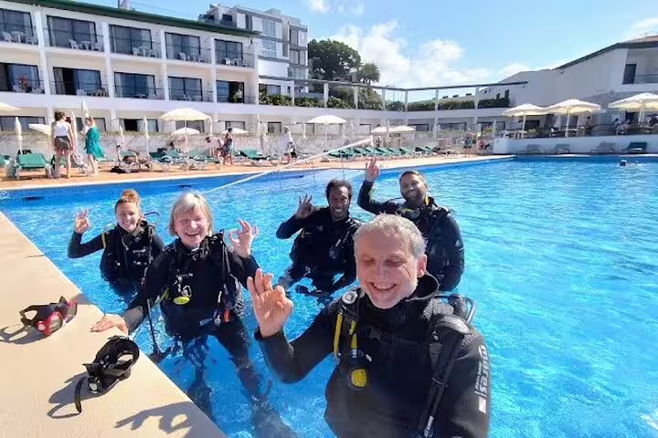 Group of happy divers in wetsuits wave from a hotel pool during an open water course, perfect for beginners seeking adventure.