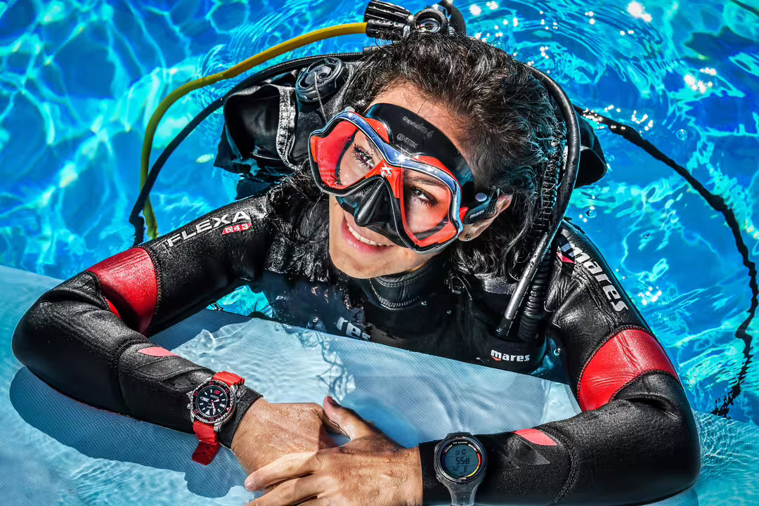 Scuba diver in a wetsuit and mask smiling at the pool's edge, promoting an open water diving course experience.