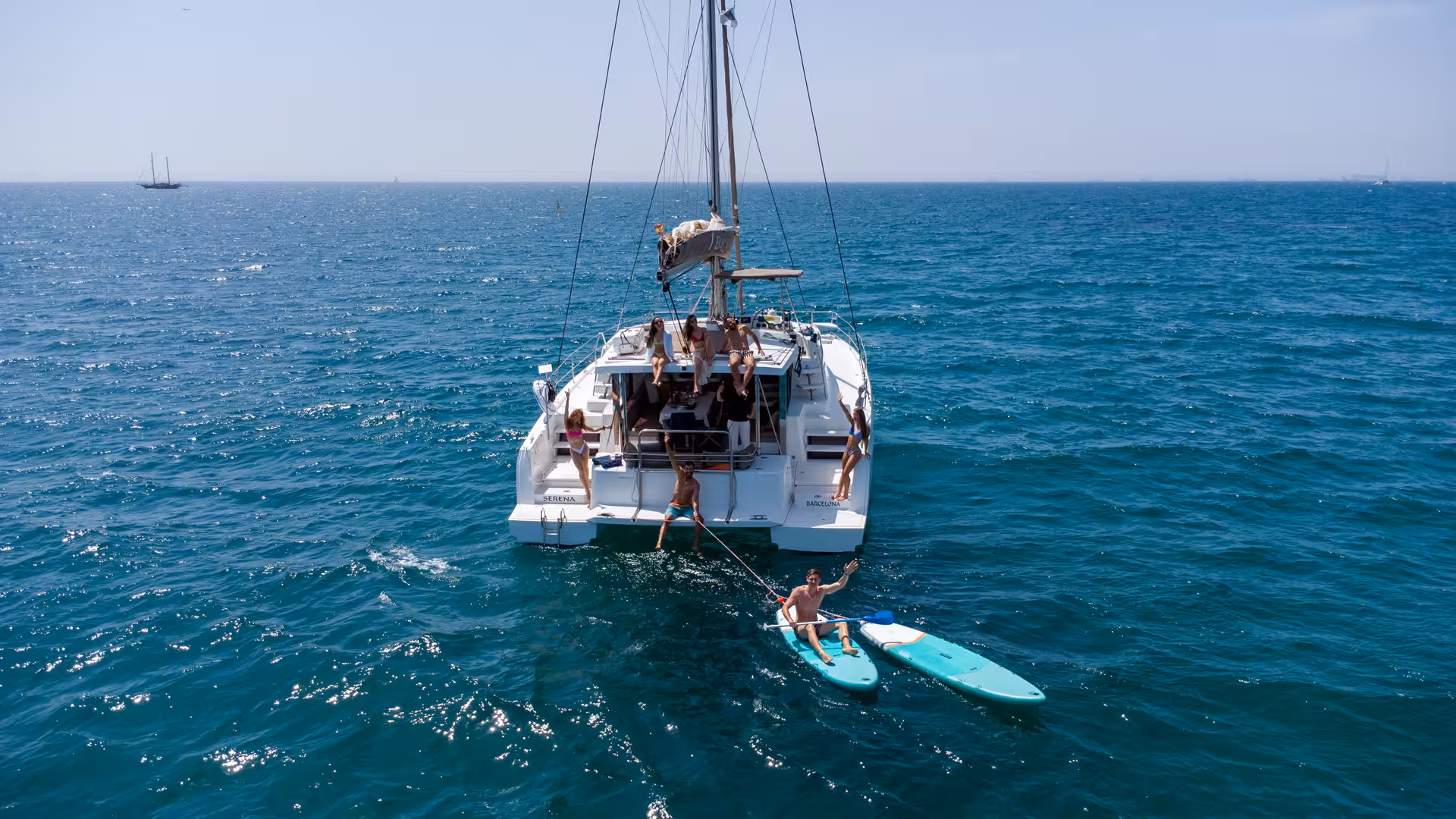 Catamaran sailing in Barcelona with guests swimming and paddleboarding, paired with a Paella Masterclass outing