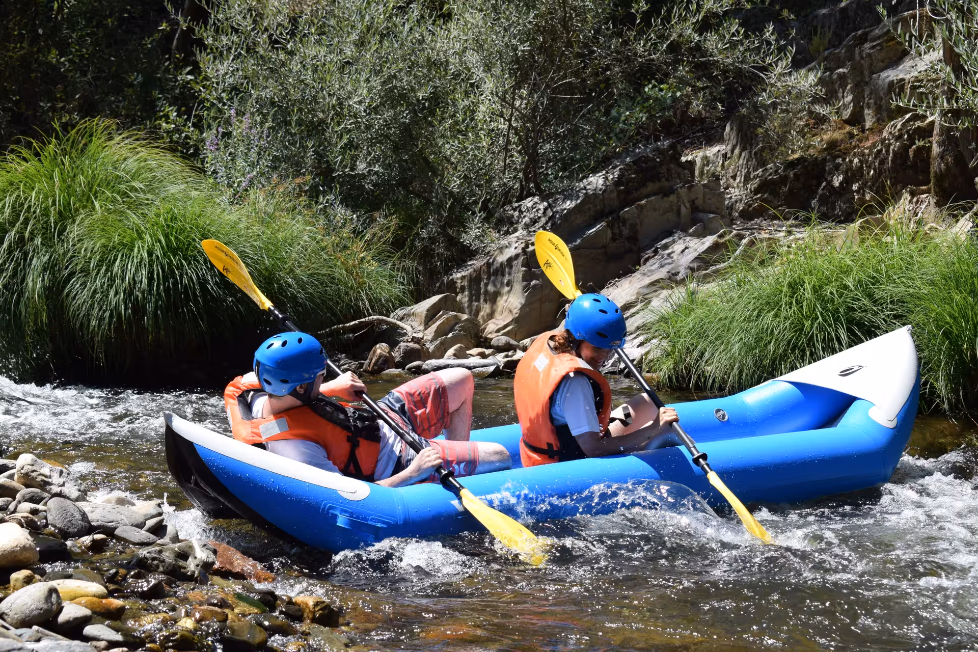 Two paddlers canoe rafting on the Paiva River, Portugal, navigating gentle rapids beside rocks and greenery