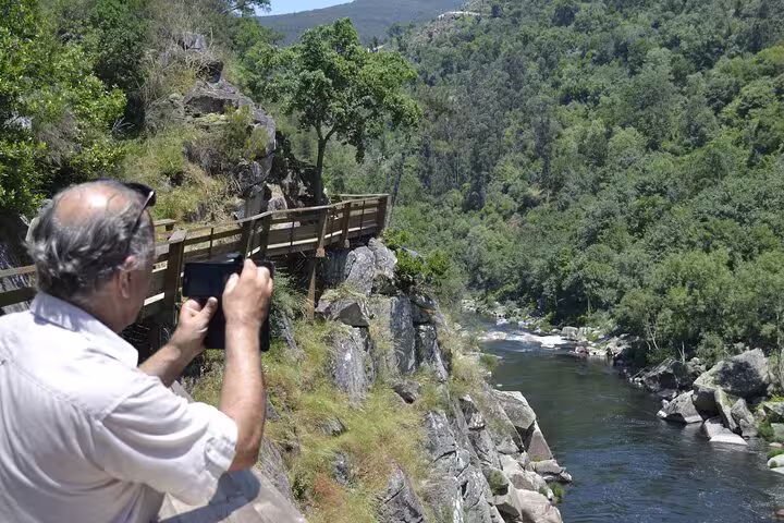A tourist captures the breathtaking river and forest views along the Paiva Walkways in Portugal with a smartphone.