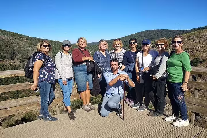Group of happy tourists enjoying a sunny day on the scenic Paiva Walkways with views of Arouca Suspension Bridge in Portugal.