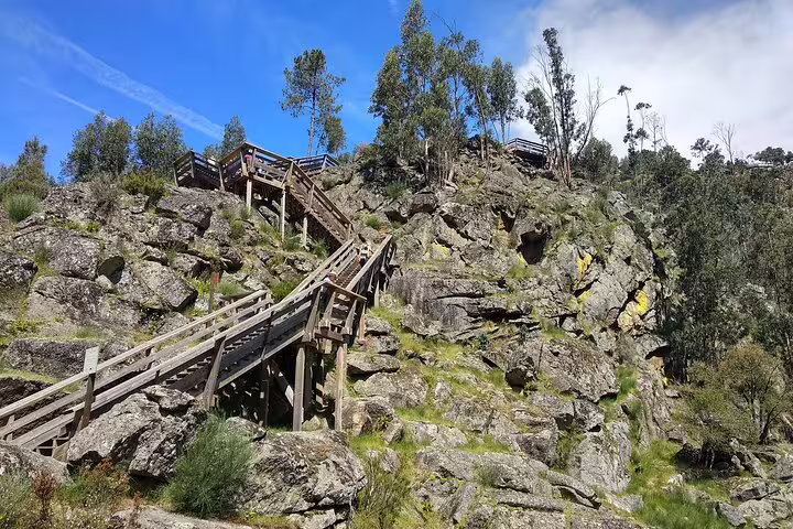 Scenic view of wooden stairs winding through rocky terrain on the Paiva Walkways, Portugal, under a clear blue sky.