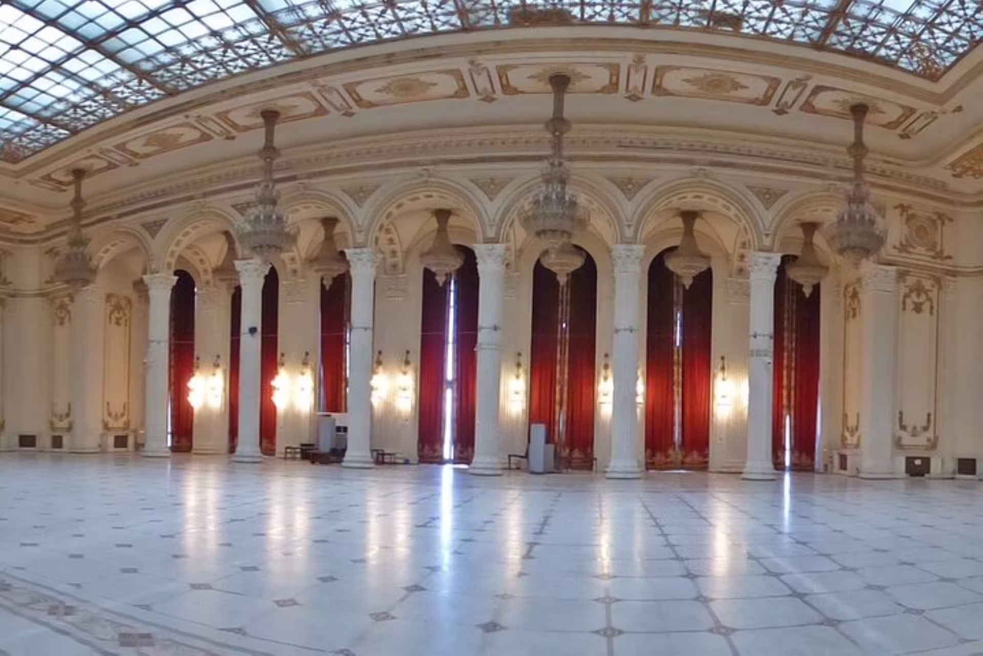 Ornate interior hall with red curtains and chandeliers at Palace of Parliament in Bucharest, ideal for Spanish tours.