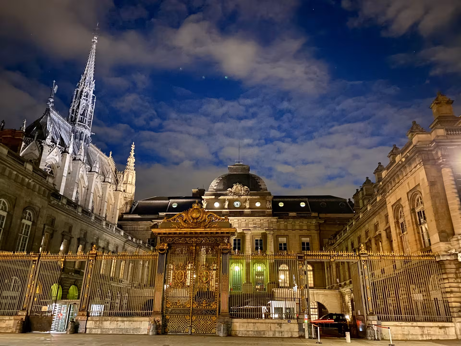 Night view of Palais de Justice in Paris with ornate gates, capturing French Revolution architecture.