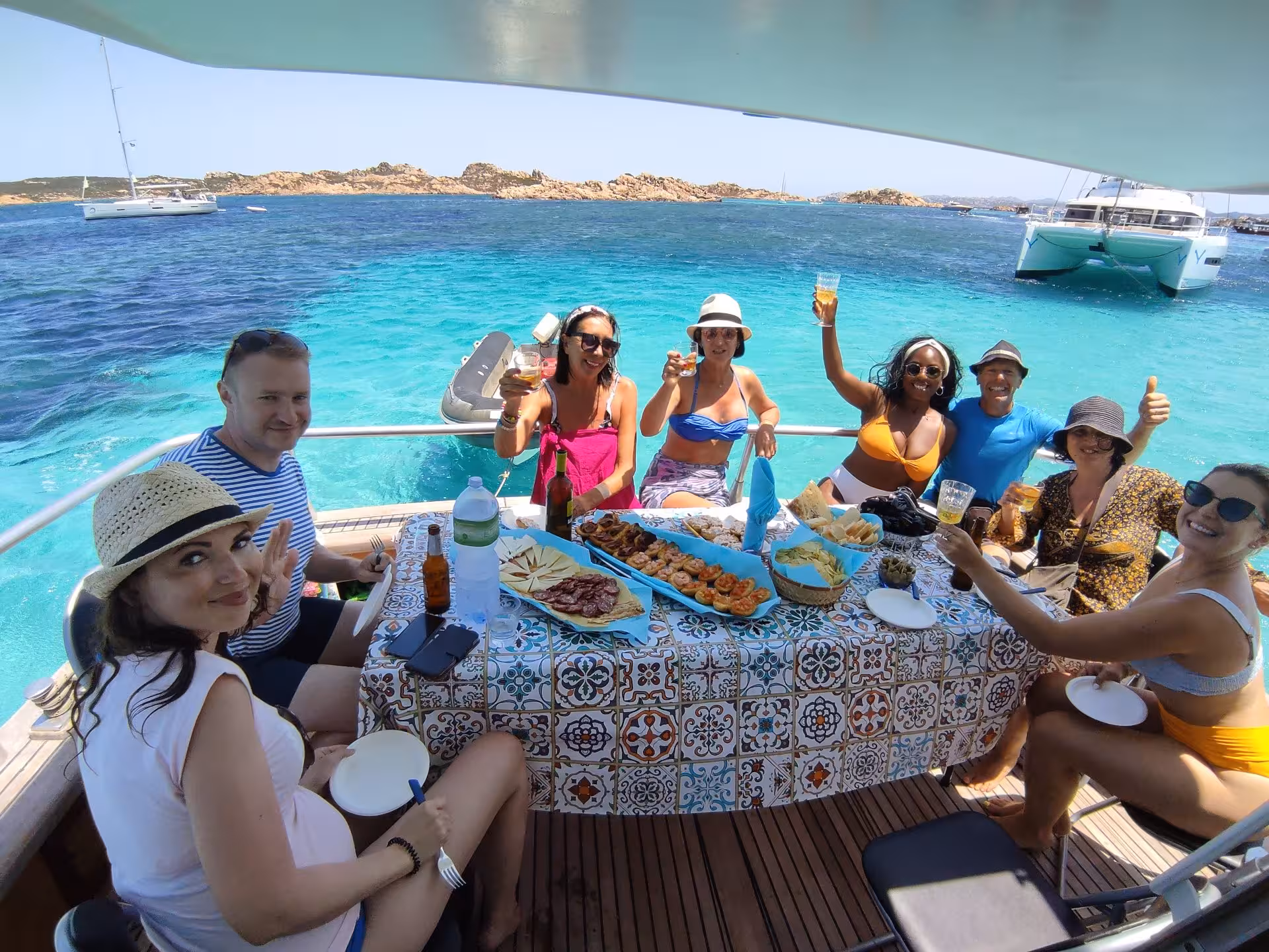Group of tourists enjoying a meal on a boat with vibrant blue waters of La Maddalena Archipelago in the background.