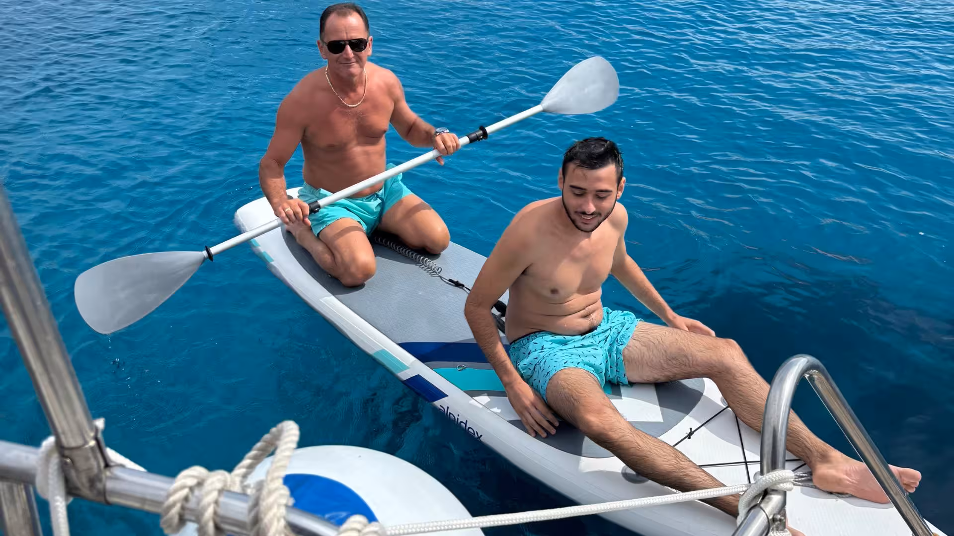 Two men paddleboarding on crystal-clear waters during a La Maddalena sailing excursion in Palau.