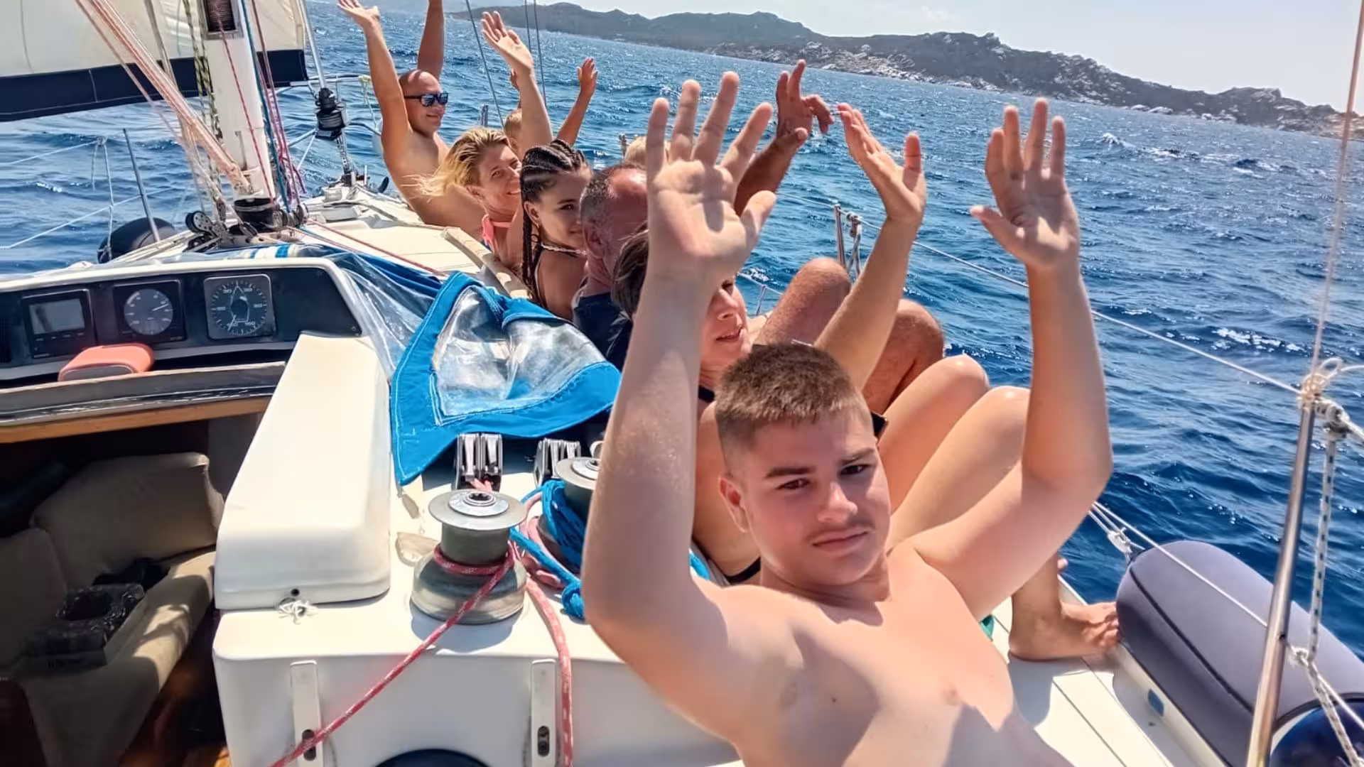 Group of people joyfully raising hands on a sailing yacht during a La Maddalena archipelago tour from Palau.
