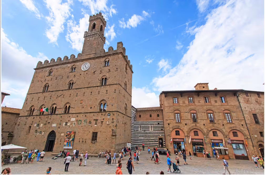 The majestic Palazzo dei Priori in Volterra stands tall against a bright sky, attracting numerous tourists.