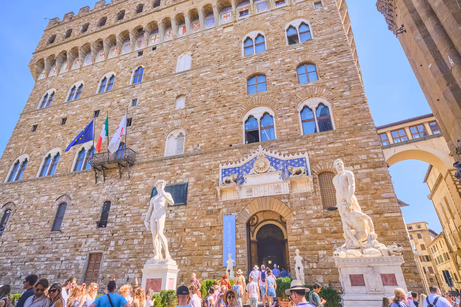 Tourists admire Palazzo Vecchio's grand facade and iconic statues on a sunny Florence walking tour.
