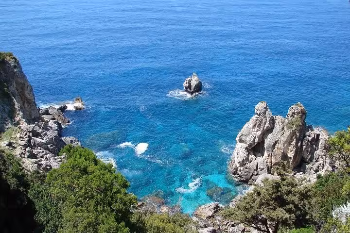 Rocky cliffs and crystal-clear blue water at Paleokastritsa, Corfu, on a private sightseeing tour with tastings