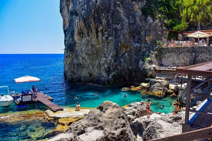 Rocky cove and turquoise water at Paleokastritsa, Corfu, with jetty and swimmers on a private tour