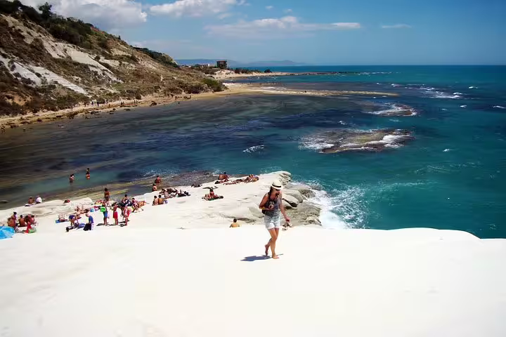 Tourist walking on the white cliffs of Scala dei Turchi near Agrigento, Sicily with turquoise sea and beachgoers below