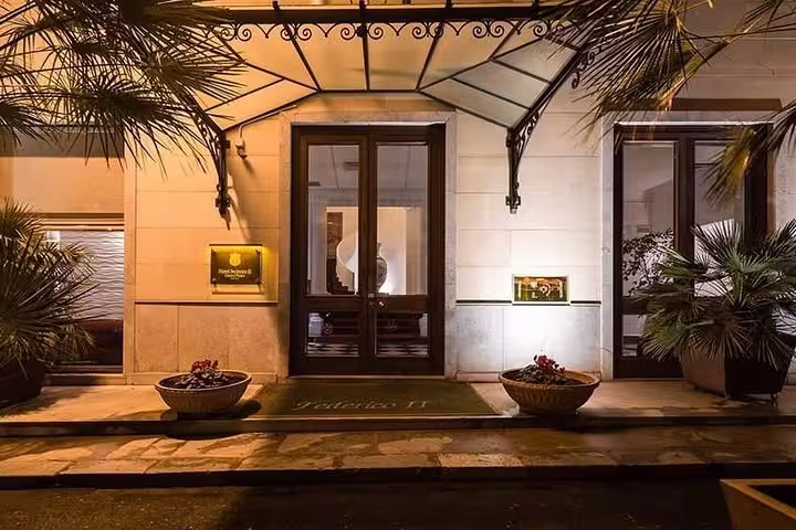 Night view of Hotel Federico II Central Palace entrance in Palermo with lit canopy, palm trees and welcome mat