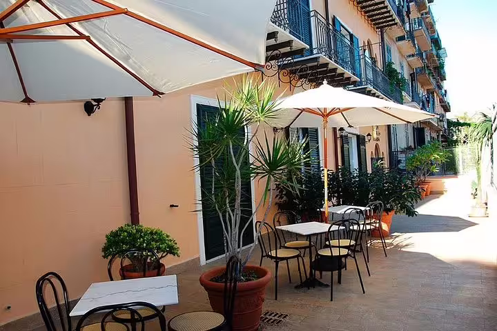 Sunny outdoor terrace at Hotel Giardino Inglese Palermo with cafe tables and umbrellas, reached by private airport transfer service