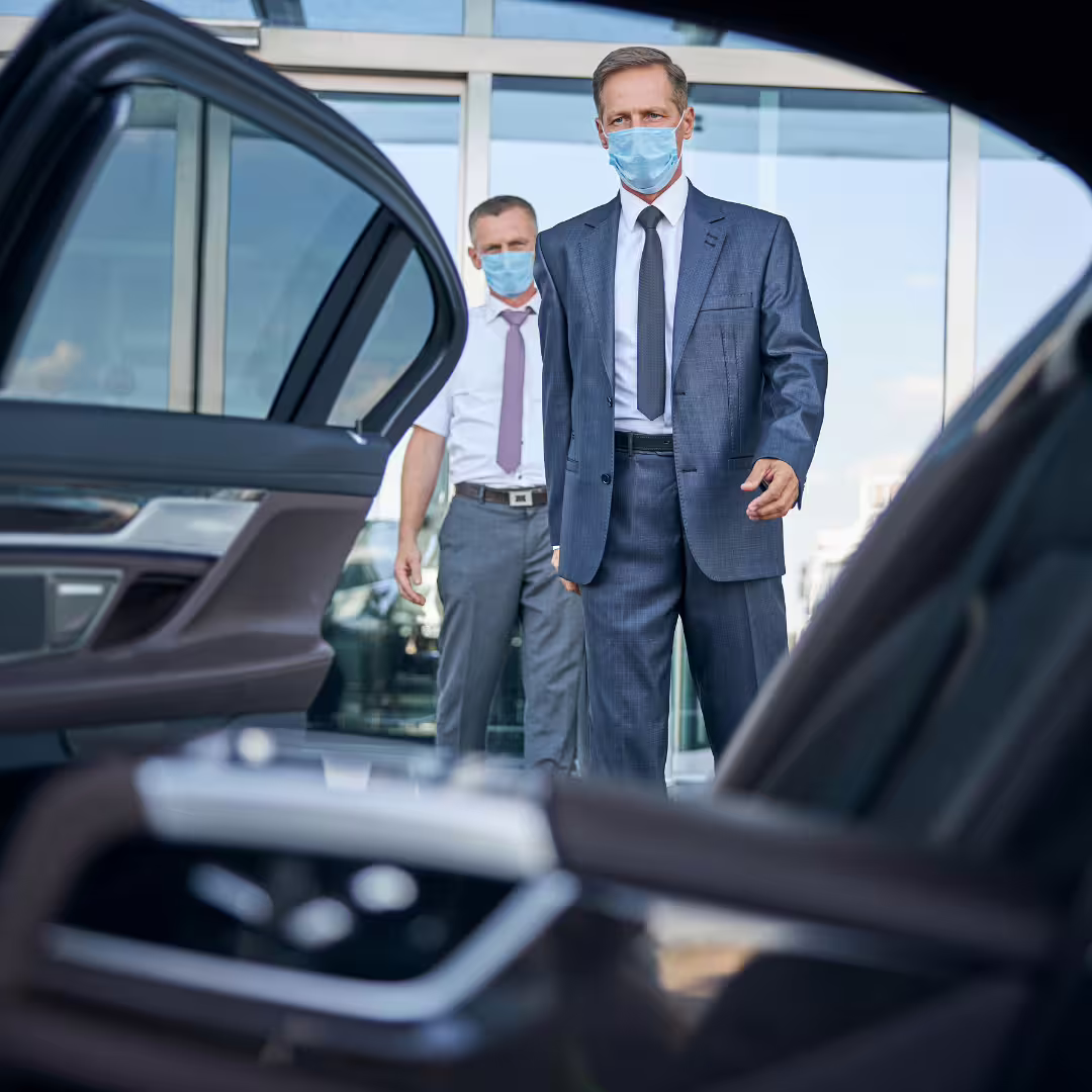 Business travelers in suits and masks boarding a luxury car for a private Palermo airport transfer to Verdura Resort Sciacca