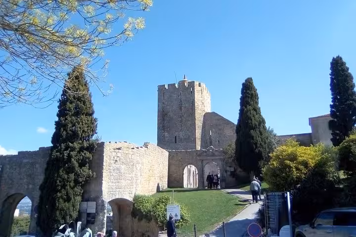 Historic Palmela Castle under a bright blue sky, surrounded by lush greenery and stone walls in Palmela, Portugal.