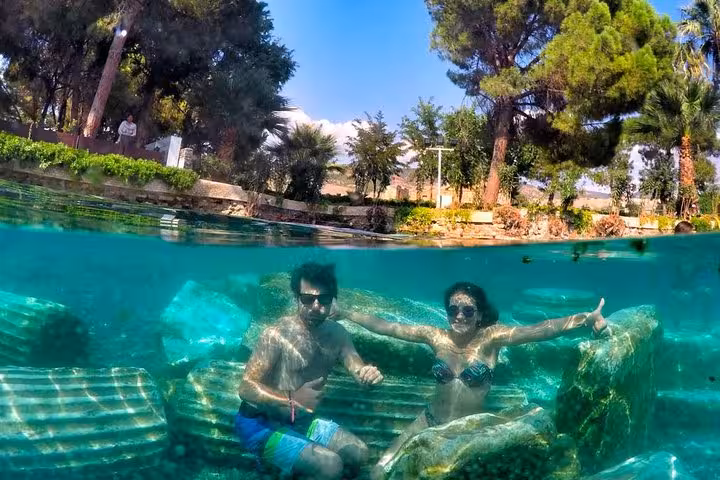Underwater view of couple swimming in Cleopatra Pool, Pamukkale, with submerged Roman columns and spa waters