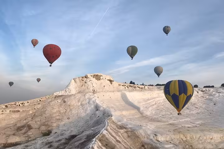 Hot air balloons floating above Pamukkale white travertine terraces at sunrise, Turkey balloon ride experience