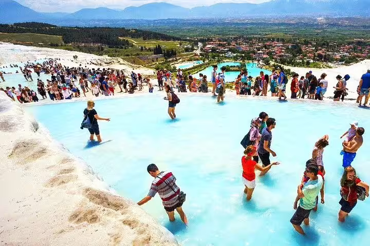 Tourists relax in the thermal pools of Pamukkale, enjoying the stunning landscape on a group tour from Izmir.