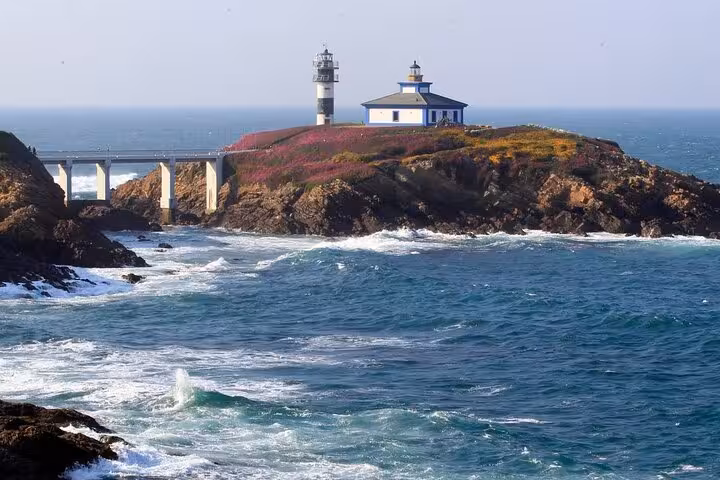 Pancha Island lighthouse on a rocky cliff surrounded by vibrant blue ocean and lush greenery, a must-see in Galicia.
