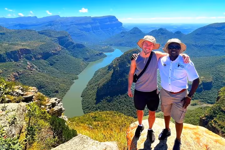 Two people enjoying a stunning panoramic view of the lush canyon and river on a sunny day during a guided tour.