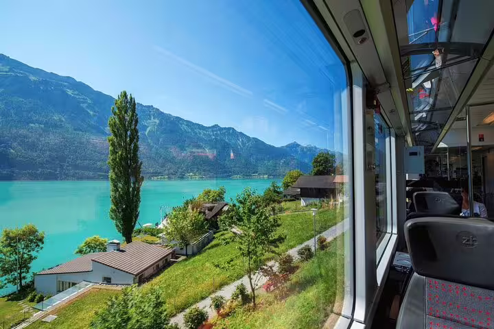 Scenic view from a panoramic train journey showcasing Swiss countryside, turquoise lake, and lush green landscapes.