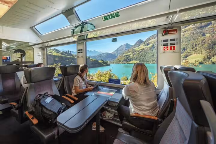 Passengers on the panoramic train admire breathtaking views of Swiss mountains and lakes, highlighting a unique journey.