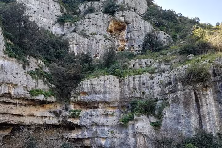 Dramatic limestone cliffs with ancient rock-cut tombs and greenery in Pantalica, Sicily.