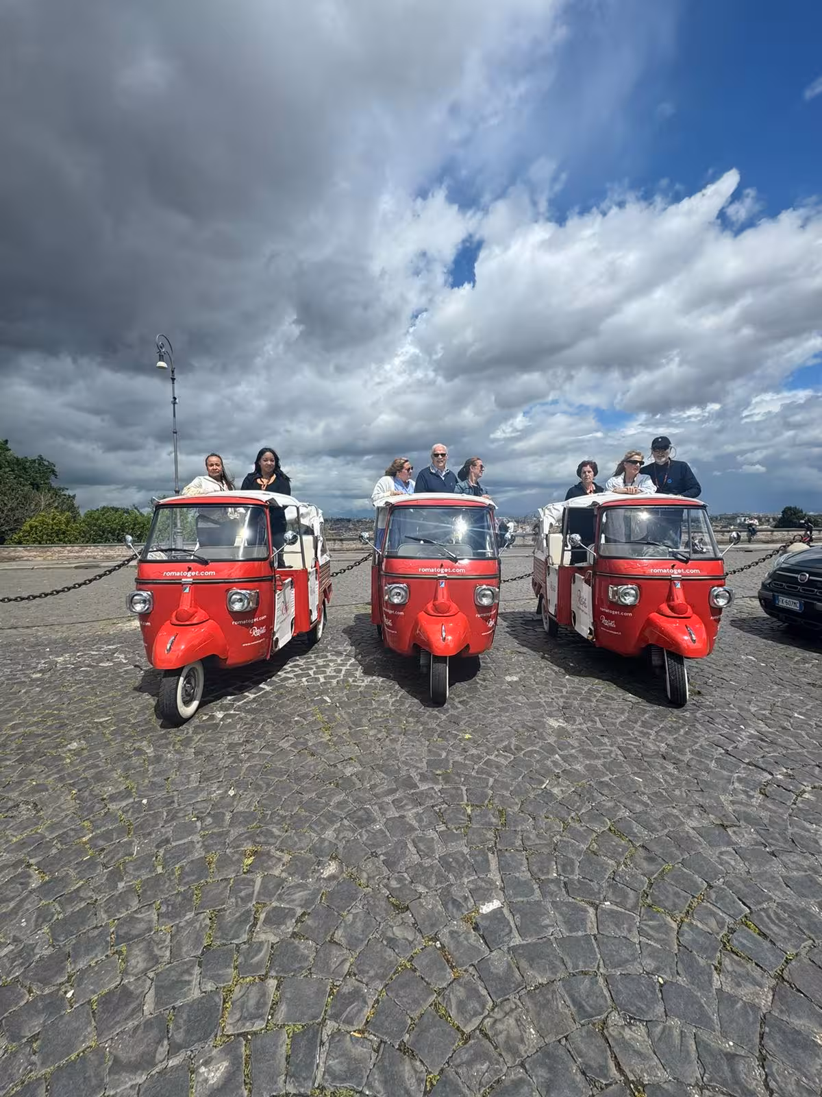 Tourists in red tuk-tuks under dramatic clouds, exploring scenic locations on the Pantheon Combo Tour.