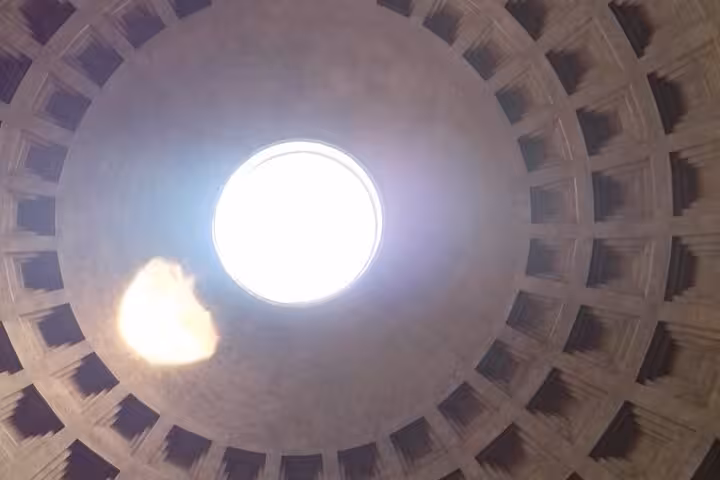 Looking up at the Pantheon's iconic oculus, sunlight streams through, highlighting the ancient dome structure.