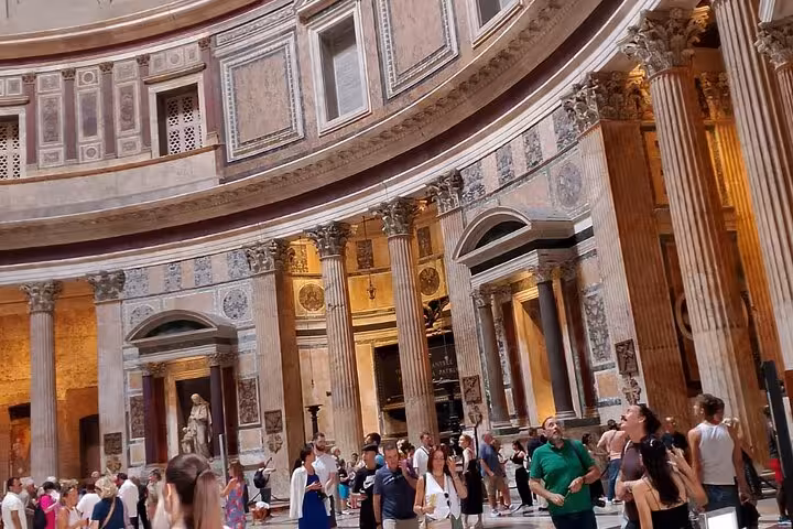 Tourists admire the majestic columns and intricate designs inside the Pantheon in Rome, capturing its historic ambiance.