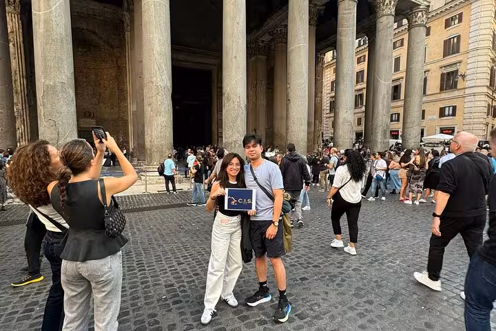 Tourists gather outside the iconic Pantheon in Rome, capturing memories with photos and a digital audio guide for an enriching experience.