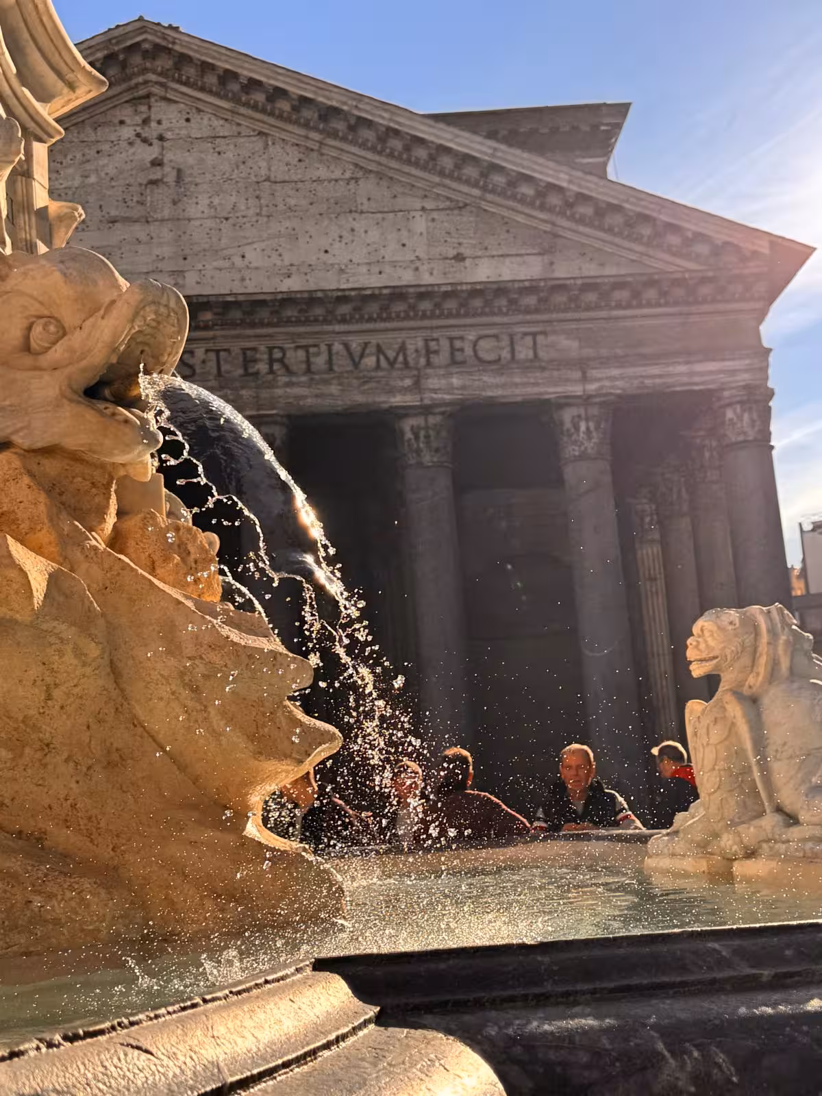 Sunlit view of the Pantheon's facade with ornate fountain in foreground, capturing Rome's historic charm and vitality.