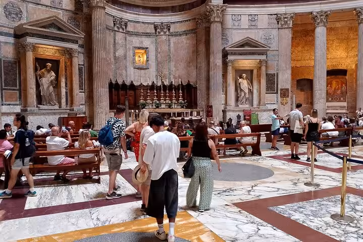 Visitors explore the grand interior of the Pantheon in Rome, featuring majestic columns and intricate statues.