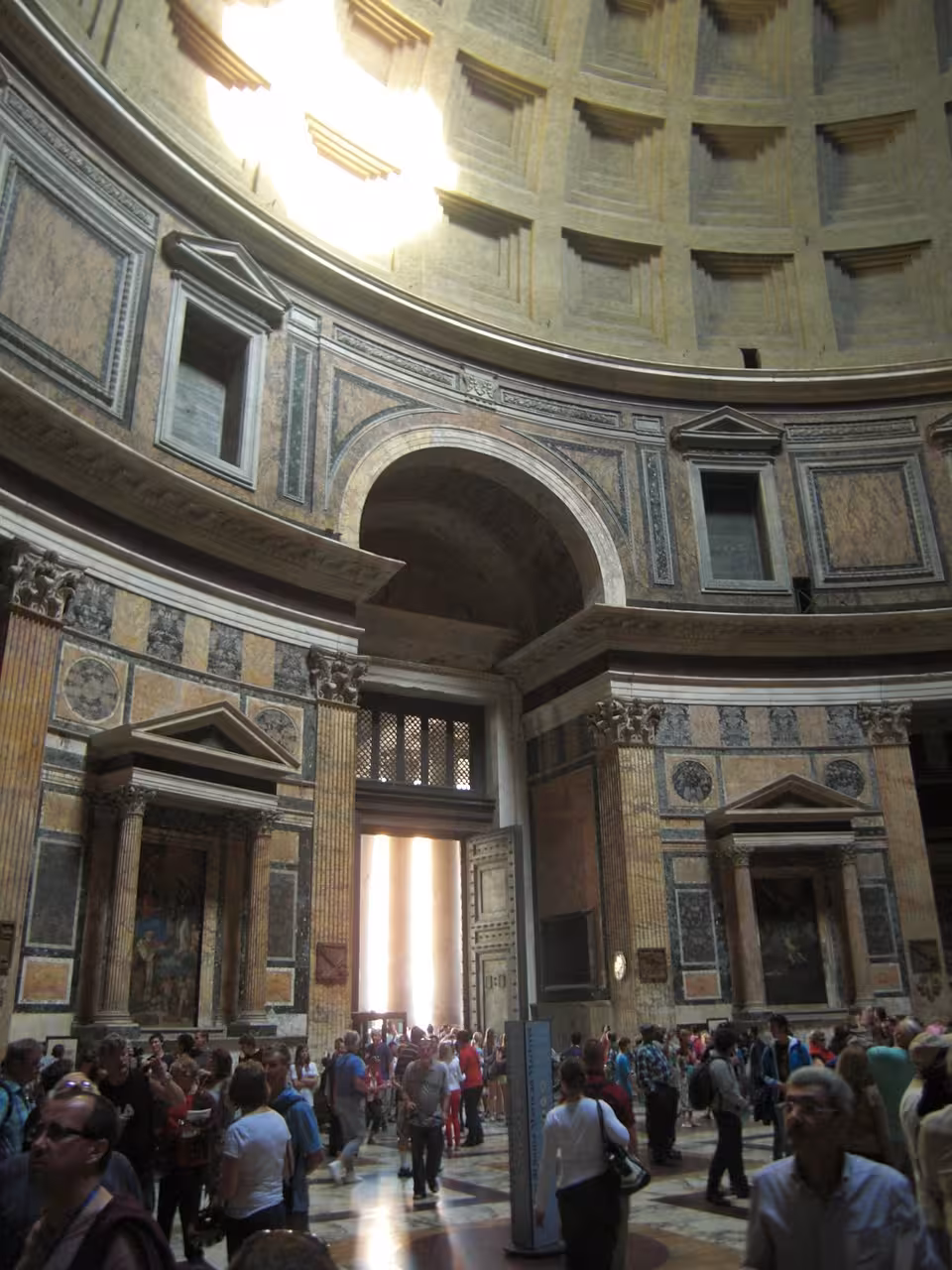 Crowd entering the Pantheon through massive doors, admiring the sunlight streaming in from the iconic oculus.