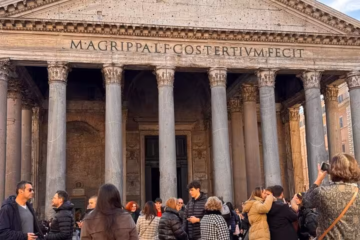 Tourists gather outside the ancient Pantheon in Rome, showcasing its grand columns and historical facade.