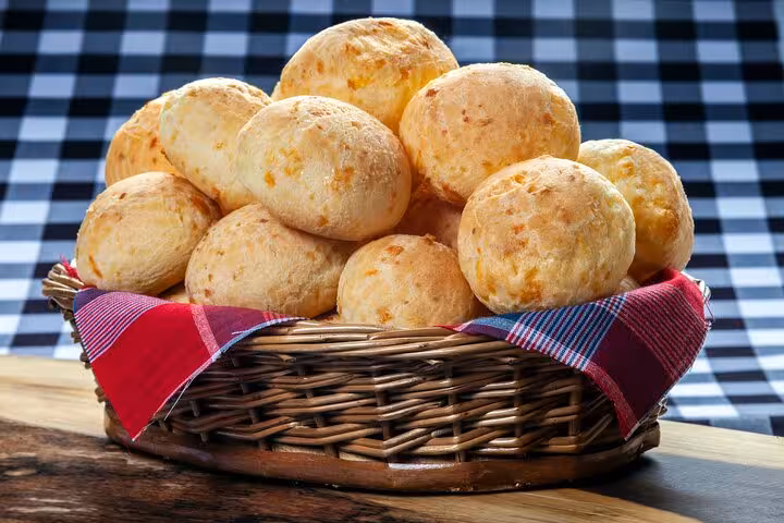 Basket of freshly baked pão de queijo on a checkered table, a tasty addition to Rio's culinary class.