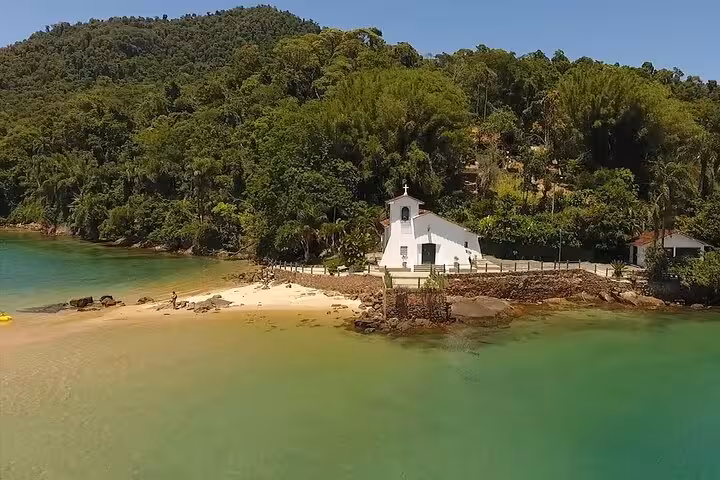 Aerial view of a serene beach with a quaint white chapel surrounded by lush greenery on Paradise Island.