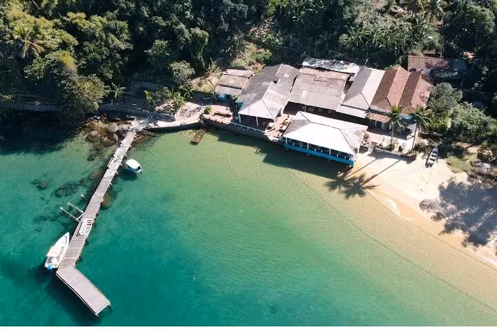Aerial shot of a serene beachfront resort with a wooden pier extending into vibrant green waters on Paradise Island.