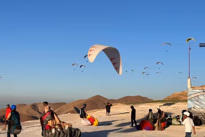 Paragliders preparing for takeoff in the Agafay Desert near Marrakech under a clear blue sky.
