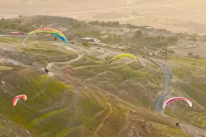 Colorful paragliders glide above the scenic Agafay Desert landscape near Marrakech, offering breathtaking aerial views.