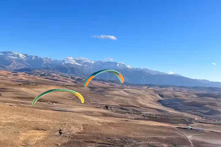 Paragliders soaring over the vast Agafay Desert in Marrakech with the Atlas Mountains in the background.